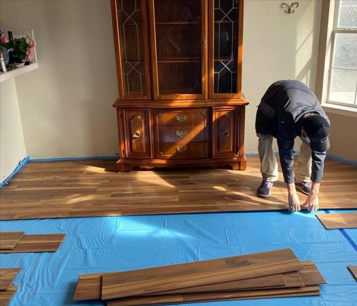 male SERVPRO employee removing wood flooring in front of large furniture